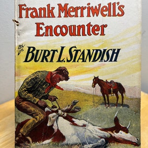 May include: A vintage book cover with an illustration of a cowboy on a horse, a cow lying on the ground, and the text "Frank Merriwell's Encounter by Burt L. Standish". The book is part of "The Merriwell Series - No. 99".