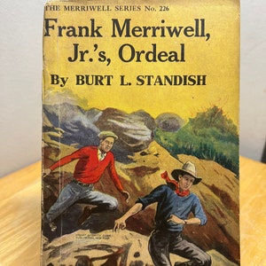 May include: A vintage book cover with a yellow background featuring an illustration of two boys running through a rocky landscape. The title is "Frank Merriwell, Jr.'s, Ordeal" by Burt L. Standish. The book is published by Street & Smith Corp. in New York.