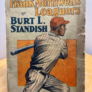 May include: A vintage book cover featuring a baseball player in a striped uniform, holding a bat. The title is "Frank Merriwell's Leaguers" by Burt L. Standish. The book is part of "The Merriwell Series" and is number 139.