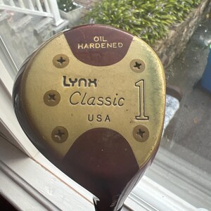 以下が含まれることがあります： 「Lynx Classic 1」と「Oil Hardened」の文字が書かれた、金色と茶色のゴルフクラブヘッド。クラブヘッドはアメリカ製です。