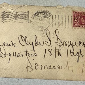 Puede incluir: Sobre antiguo con un sello rojo de dos centavos y un matasellos de 1903. El sobre está dirigido al teniente Clyde I. Srauer, con texto manuscrito y una ilustración de bandera.