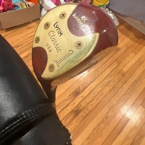 以下が含まれることがあります： 茶色の木製シャフトと金色のヘッドを持つビンテージゴルフクラブ。ヘッドには「Lynx Classic 1 USA」と「Oil Hardened」の文字が書かれています。