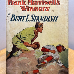May include: A vintage book cover with a baseball theme. The cover features an illustration of two baseball players in action. The title of the book is "Frank Merriwell's Winners" by Burt L. Standish. The book is part of "The Merriwell Series" and is numbered No. 88.