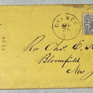 Może przedstawiać: Żółta, zabytkowa koperta z odręcznym pismem i niebieskim znaczkiem pocztowym. Koperta jest zaadresowana do Rev. Chas. E. Knott w Bloomfield, New Jersey, i opatrzona datą 26 kwietnia 1870 r. Koperta jest podarta na prawym brzegu.