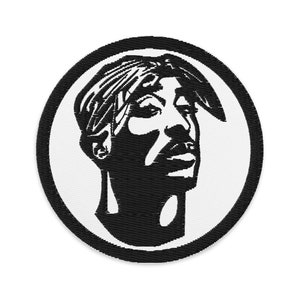 May include: A circular embroidered patch featuring a high-contrast black and white graphic portrait of a person wearing a bandana. The design is rendered in black thread against a white background, enclosed by a thick black stitched border.