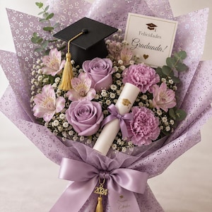 May include: A graduation bouquet featuring lavender roses, pink alstroemeria, and carnations, accented with baby's breath and eucalyptus. The bouquet includes a miniature graduation cap, a rolled diploma, and a card that reads "Felicidades Graduada!" The bouquet is wrapped in lavender paper and tied with a matching ribbon.