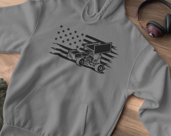 May include: Grey hoodie with a black race car graphic and an American flag design. The hoodie has a front pocket, a hood with drawstrings, and long sleeves. Also visible are a green beanie, black shoes, and headphones.