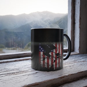 May include: Black coffee mug with a white and red American flag design and a silhouette of a race car. The mug has a black handle.