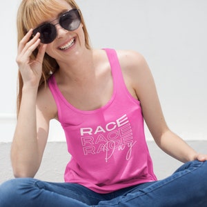 Puede incluir: Un top de tirantes rosa con el texto "RACE DAY" impreso en blanco. El texto está apilado y estilizado con una ligera inclinación.