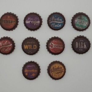 May include: Twelve different bottle caps featuring various Nuka Cola flavours, including Sunset Sarsaparilla, Grape, Cherry, Wild, Dark, and Orange. The caps are all brown with white and gold lettering.