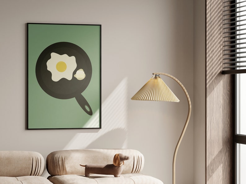 Puede incluir: Una impresi&oacute;n enmarcada con una ilustraci&oacute;n minimalista de un huevo frito en una sart&eacute;n sobre un fondo verde claro. La obra de arte est&aacute; en un marco negro y cuelga sobre un sof&aacute; beige. Un perro salchicha decorativo y una l&aacute;mpara de pie tambi&eacute;n est&aacute;n en la imagen.