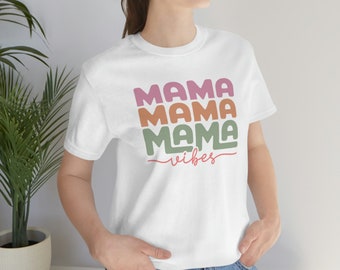 Puede incluir: Camiseta blanca con el texto "Mama Mama Mama vibes" en rosa, naranja y verde.