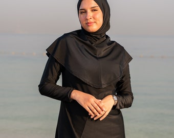 May include: A black long-sleeved swimsuit with a hood, worn by a person standing on a beach.