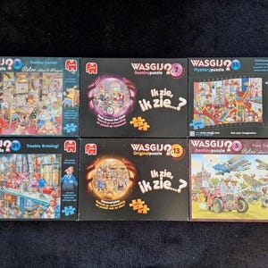 Può includere: Sei scatole di puzzle misteriosi Wasgij. Le scatole presentano illustrazioni colorate con il logo Wasgij e titoli come "Sunday Lunch!" e "Trouble Brewing!". I puzzle sono progettati per l'intrattenimento.