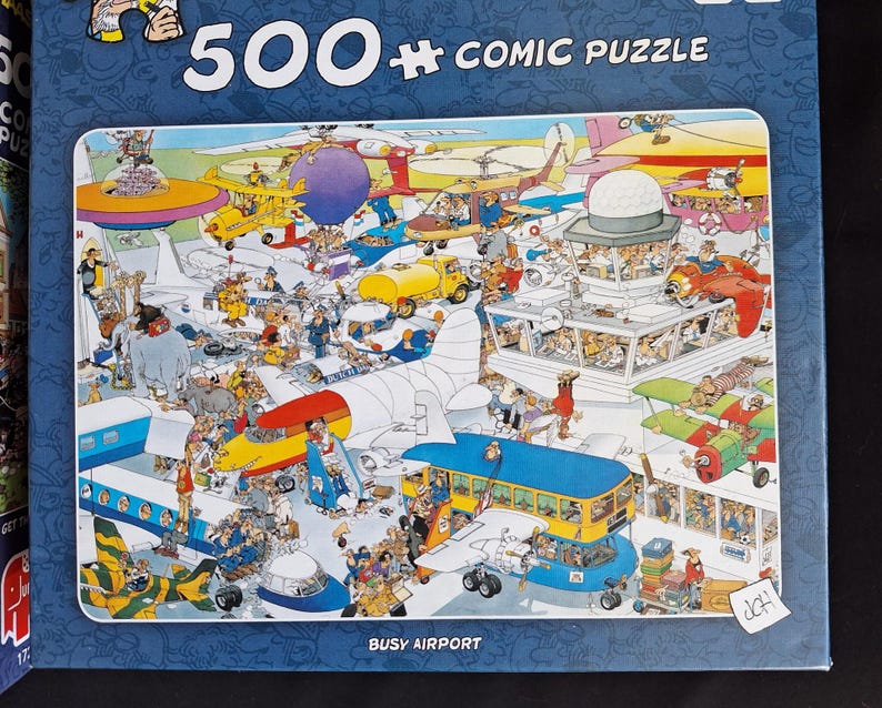 Puede incluir: Un rompecabezas c&oacute;mico de 500 piezas que representa un aeropuerto concurrido. La imagen muestra numerosos aviones, veh&iacute;culos y personas en un estilo colorido y de dibujos animados. El texto "BUSY AIRPORT" es visible en la parte inferior.