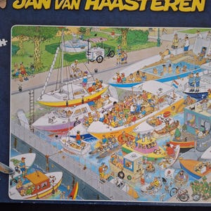 May include: A 1000+ piece comic puzzle by Jan van Haasteren. The image shows a bustling harbour scene with many boats, people, and a food cart. The puzzle box has text in multiple languages, including English, Dutch, and French.