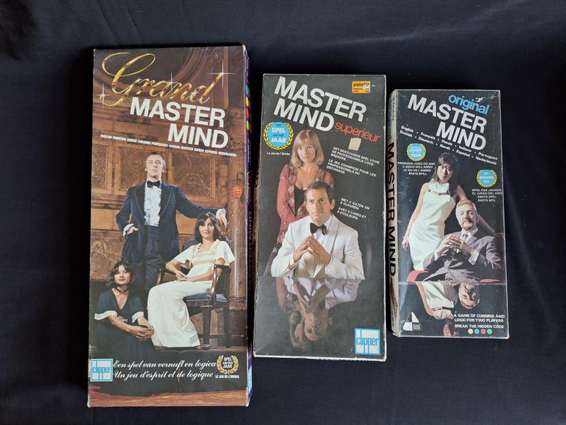 May include: Three vintage Master Mind board game boxes. The boxes feature images of people in formal attire. The largest box is labeled "Grand Master Mind" and includes text in multiple languages. The other two boxes are labeled "Master Mind" and "original Master Mind".