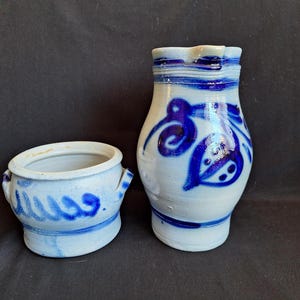 May include: A set of two blue and white ceramic pottery pieces. A jug with a blue floral design and a small bowl with a blue and white swirl design.