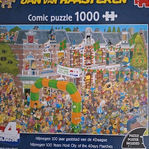 May include: A 1000-piece jigsaw puzzle with a detailed comic illustration of a bustling street scene. The puzzle includes text that reads "Comic puzzle 1000+" and "Nijmegen 100 jaar gaststad van de 4Daagse". The image is filled with people, buildings, and an archway.