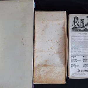 May include: Three vintage game boxes are displayed. The boxes are rectangular and made of cardboard. The boxes are off-white with some discoloration. One box has text in multiple languages, including English, French, and German. The boxes are empty.