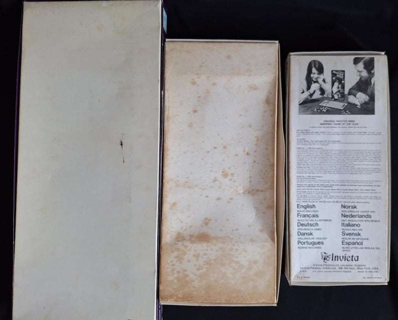 May include: Three vintage game boxes are displayed. The boxes are rectangular and made of cardboard. The boxes are off-white with some discoloration. One box has text in multiple languages, including English, French, and German. The boxes are empty.