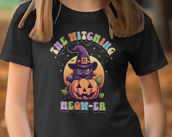 Op de afbeelding: Zwart T-shirt met een afbeelding van een zwarte kat met een heksenhoed en een jack-o'-lantern. De tekst "The Witching Meow-er" is geschreven in regenboogkleuren.
