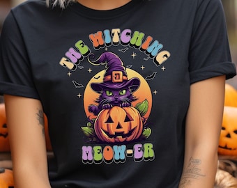 Op de afbeelding: Zwart T-shirt met een afbeelding van een zwarte kat met een heksenhoed en een jack-o'-lantern. De tekst "The Witching Meow-er" is geschreven in regenboogkleuren.