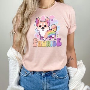 Puede incluir: Una camiseta rosa con un chihuahua de dibujos animados que lleva una cola arco&iacute;ris y el texto "PAWride" en letras arco&iacute;ris.