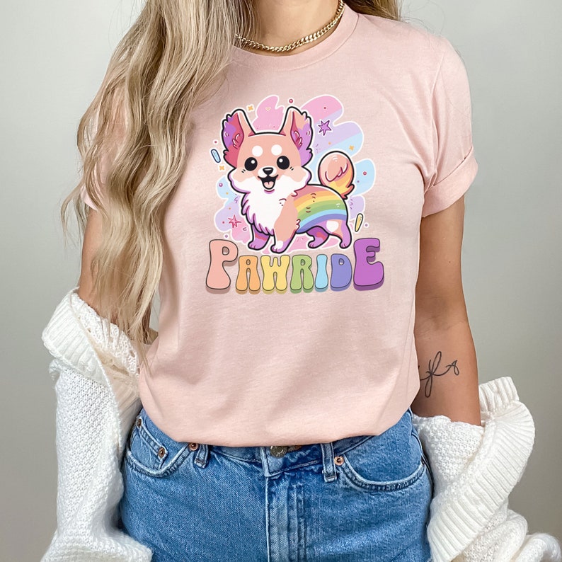 Puede incluir: Una camiseta rosa con un chihuahua de dibujos animados que lleva una cola arco&iacute;ris y el texto "PAWride" en letras arco&iacute;ris.