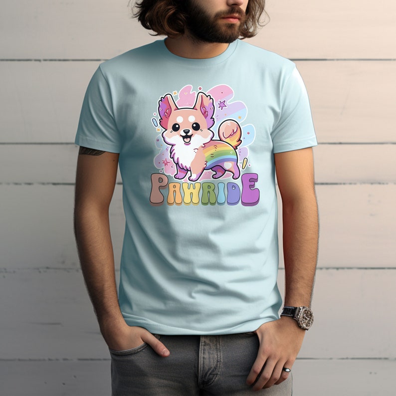 Puede incluir: Una camiseta azul claro con una imagen de dibujos animados de un perro con una cola de arco&iacute;ris. El texto "PAWRIDE" est&aacute; impreso en colores arco&iacute;ris debajo del perro.