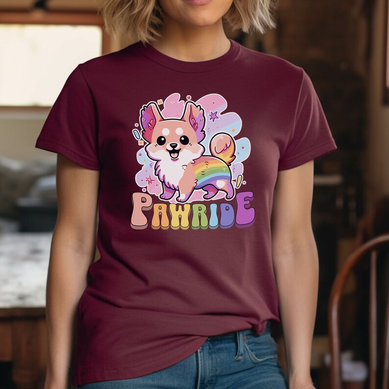 Puede incluir: Una camiseta color burdeos con una imagen de dibujos animados de un perro con una cola arco&iacute;ris. El texto "PAWRIDE" est&aacute; impreso en colores arco&iacute;ris debajo del perro.