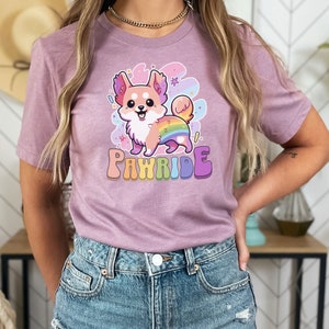 Puede incluir: Una camiseta morada con un perro de dibujos animados que lleva un arco&iacute;ris en la espalda. El texto "PAWRIDE" est&aacute; impreso debajo del perro.