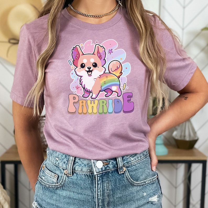 Puede incluir: Una camiseta morada con un perro de dibujos animados que lleva un arco&iacute;ris en la espalda. El texto "PAWRIDE" est&aacute; impreso debajo del perro.