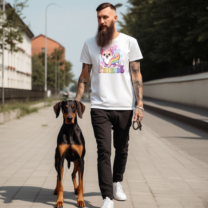 Puede incluir: Un hombre lleva una camiseta blanca con un perro de dibujos animados y el texto "Pawrade" impreso en ella. Camina con un perro negro y marr&oacute;n con una correa.