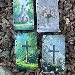 Può includere: Quattro inserti decorativi per planner con immagini ad acquerello. Uno mostra una chiesa, un altro un vaso di fiori e due presentano croci in ambienti naturali. Ogni inserto ha fori preforati per la rilegatura.
