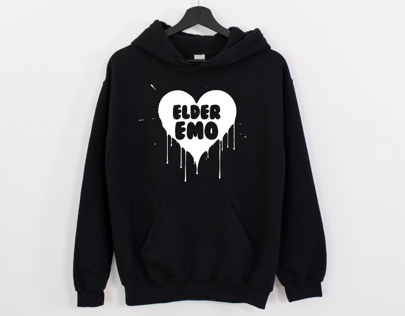 K&ouml;nnte beinhalten: Schwarzer Kapuzenpullover mit einem wei&szlig;en Herz-Motiv, auf dem "Elder Emo" in einem tropfenden Farbstil steht.