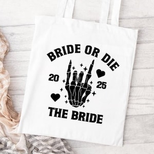 May include: White tote bag with black text and graphics. The text reads "BRIDE OR DIE" above a black skeleton hand making a rock and roll gesture. Below the hand is the text "THE BRIDE", with the numbers "20" and "25" on either side.