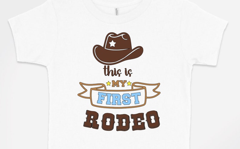 Pode incluir: Camiseta branca com um chap&eacute;u de cowboy marrom, uma faixa marrom com o texto "This is my first rodeo" em letras amarelas, azuis e marrons.
