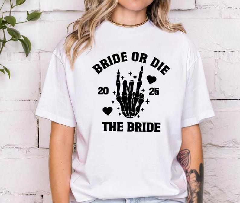 May include: White t-shirt with a black graphic that reads "BRIDE OR DIE" above a skeleton hand making a rock-and-roll gesture. The text "20 25" and "THE BRIDE" are also in black. Two black hearts and stars complete the design.
