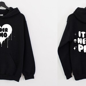K&ouml;nnte beinhalten: Schwarzer Kapuzenpullover mit einem wei&szlig;en Herzdesign, auf dem "Elder Emo" steht und Farbe tropft. Die R&uuml;ckseite des Pullovers hat einen wei&szlig;en Text, der "It was never a phase" mit Sternen und Alien-Gesichtern sagt.