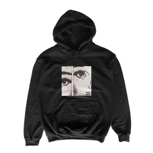 Peut inclure: Sweat-shirt à capuche noir avec un imprimé graphique d'une image de style bande dessinée de deux yeux, dont un avec une larme. Le texte "Parental Advisory" est imprimé sur l'image.