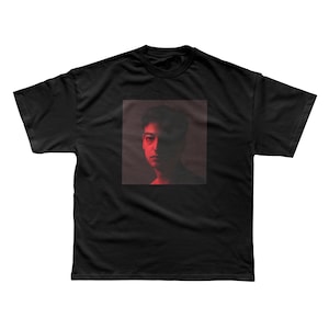 May include: A black t-shirt featuring a red image of a person's face.