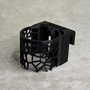 Puede incluir: Portavasos negro impreso en 3D con un diseño geométrico. El portavasos tiene un gancho en el lateral para colgarlo.