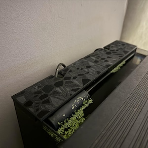 Puede incluir: Un acuario rectangular negro con tapa estampada y asa met&aacute;lica. El acuario contiene plantas acu&aacute;ticas y un filtro cil&iacute;ndrico negro. El dise&ntilde;o presenta formas geom&eacute;tricas y una est&eacute;tica elegante y moderna.