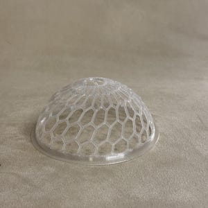 May include: A clear plastic dome shaped like a half sphere with a hexagonal pattern.