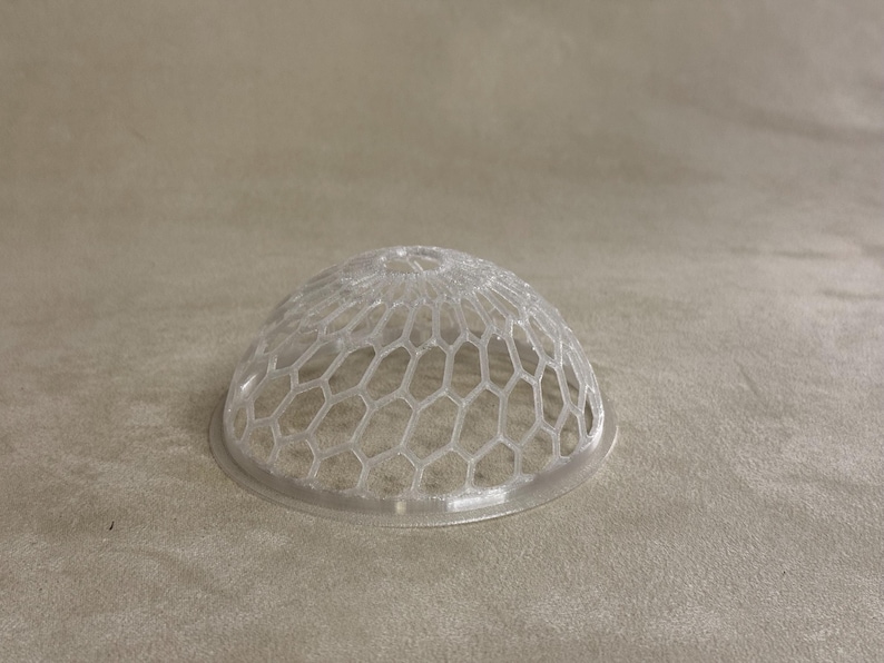 May include: A clear plastic dome shaped like a half sphere with a hexagonal pattern.