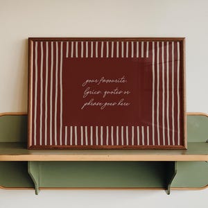 May include: A rectangular framed print with a dark red background and white vertical stripes on the left and right sides. The centre features the white cursive text: your favourite. lyrics, quotes or phrase goes here. The frame is dark brown wood.