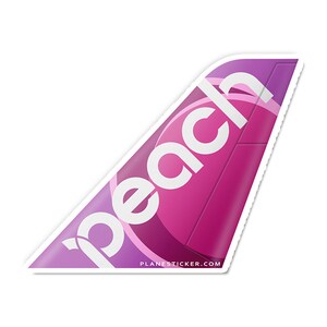 May include: A pink and purple airplane tail fin sticker with the word "Peach" in white lettering. The sticker is designed to look like a real airplane tail fin.