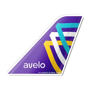 May include: Purple airplane tail fin sticker with a white, yellow, and blue geometric design. The sticker has the word "avelo" in white text and the website "PLANESTICKER.COM" in smaller white text.