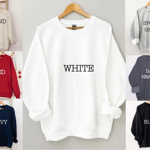 May include: A white sweatshirt with the word "WHITE" printed on the front. The sweatshirt is available in 10 colors: sand, red, navy, black, sport grey, dark heather, white, light heather, pink, and teal.